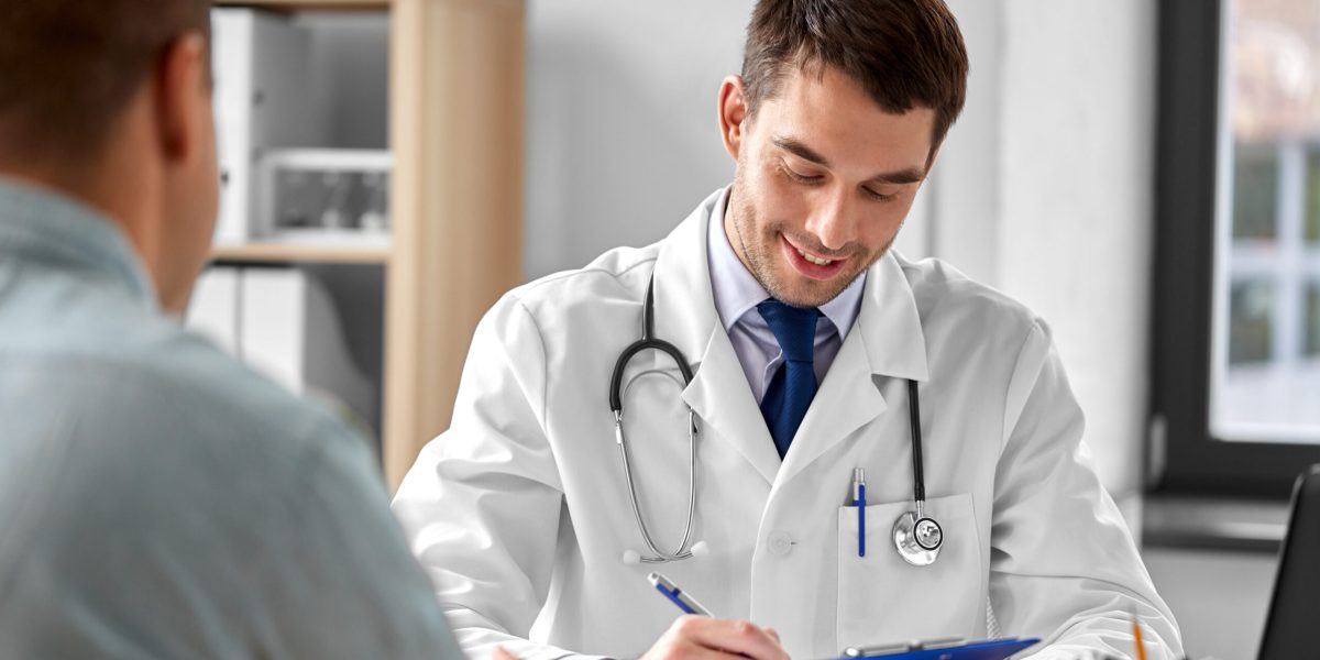 medicine, healthcare and people concept - doctor with clipboard talking to male patient at medical office in hospital